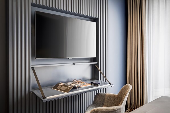 A modern living room with a mounted TV, a magazine on a shelf, and a chair. - Kyriad Lyon Ouest - Limonest (Limonest)