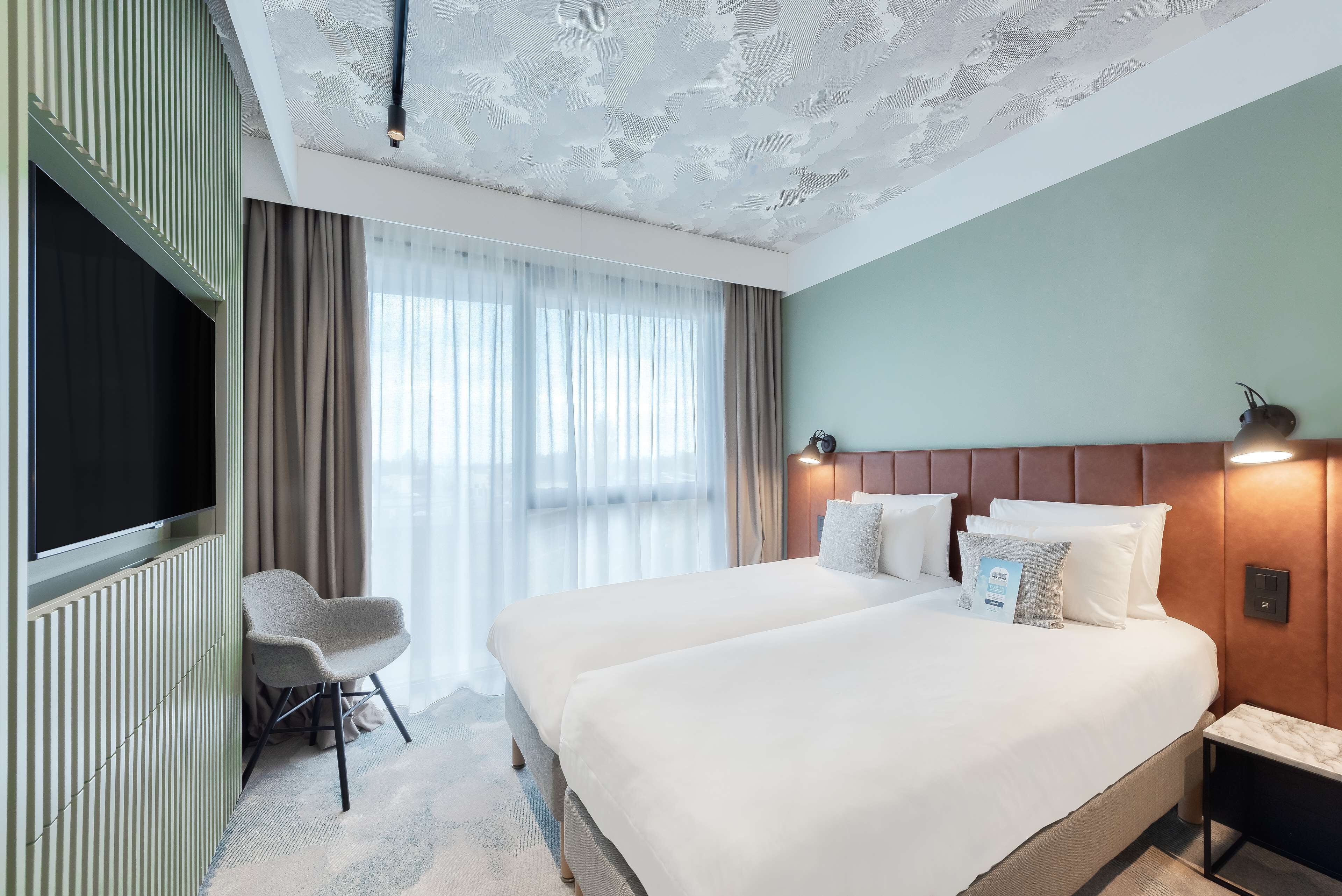 A hotel room with a large bed, a TV, a seating area, and a window with curtains.