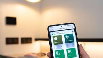 Ein Smartphone zeigt eine Smart-Home-App mit Optionen zur Lüftung, Temperaturregelung, Kino-Modus und Energieeinstellungen.