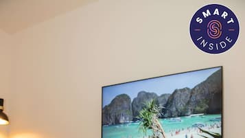 A person lying on a bed in a room with a television displaying a beach scene, a bedside table with a lamp, and a wall-mounted picture.