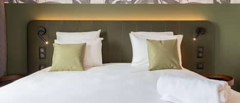 A neatly made bed with white linens and two pillows, one green and one white, in a room with a green headboard and wall art.