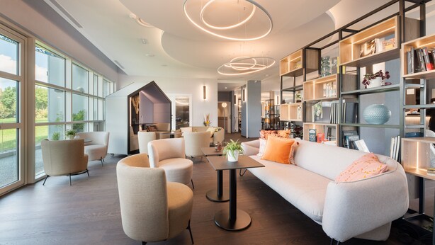 Een moderne woonkamer met een bank, fauteuils en een salontafel. Er staan boekenkasten met boeken en decoratieve objecten.
