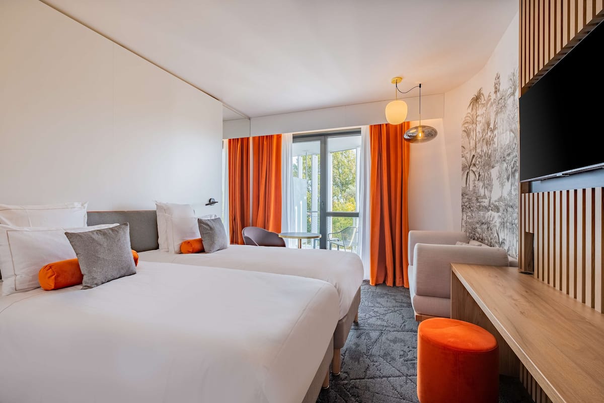 A modern hotel room with two beds, a desk, and a TV.