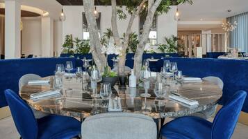 Un coin repas avec une table ronde dressée pour quatre personnes, entourée de chaises recouvertes d’un tissu bleu.