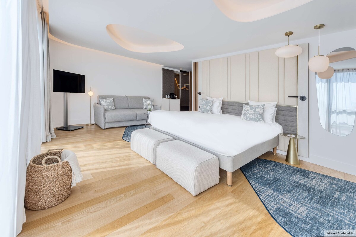 Une chambre moderne avec un grand lit, un canapé, une armoire et un téléviseur à écran plat.