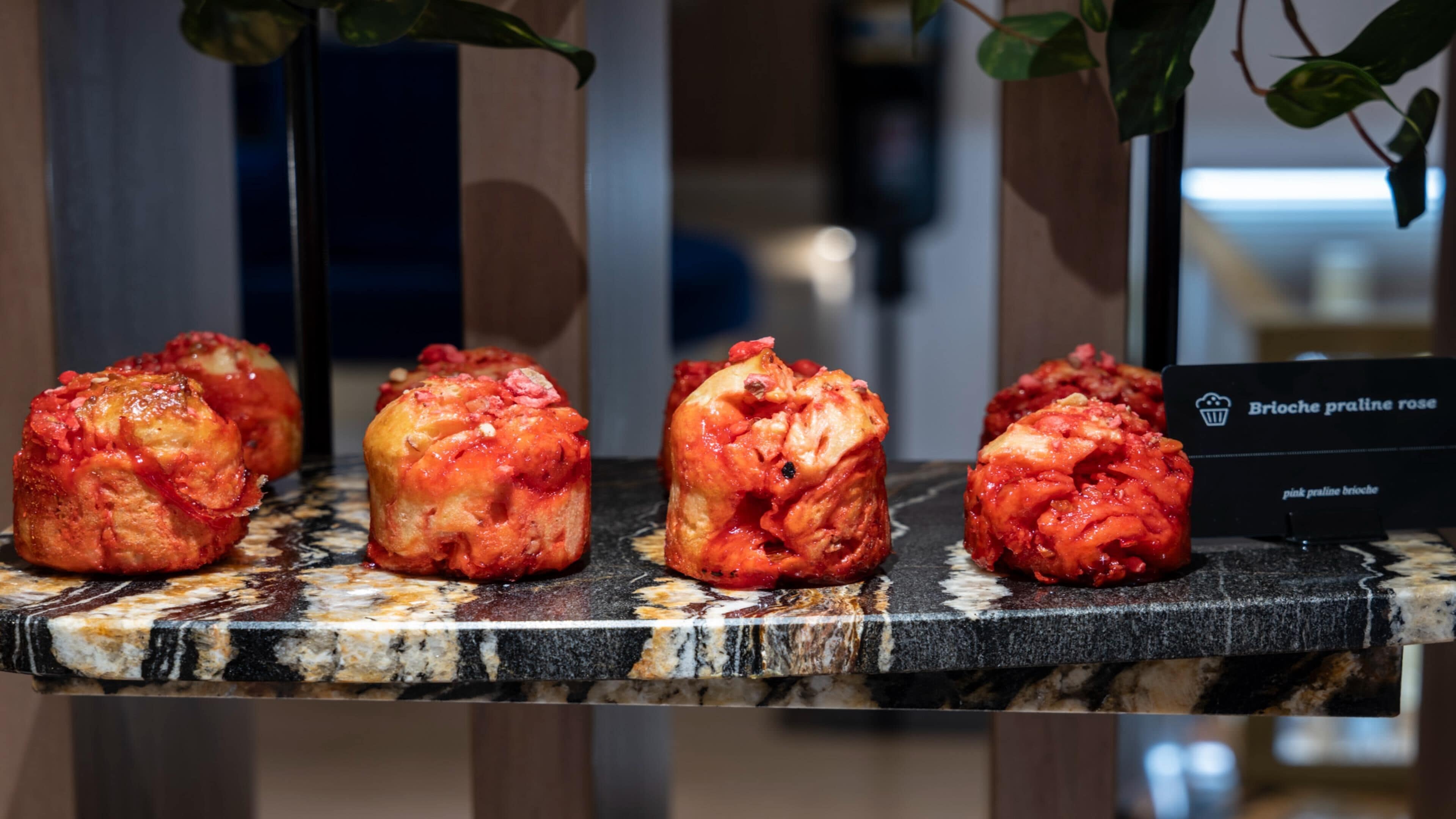 Une présentation de viennoiseries à la brioche et à la crème pralinée rose, disposées sur un comptoir en marbre.