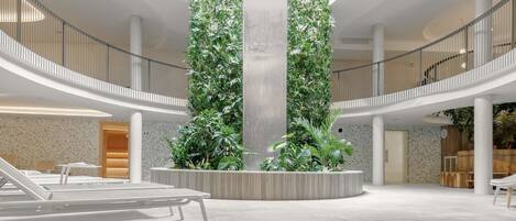 A spacious indoor area with a central column, surrounded by seating and greenery.