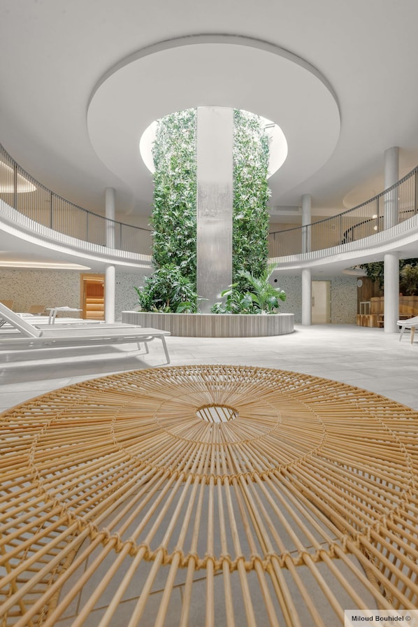 A spacious indoor area with a central column, surrounded by seating and greenery.