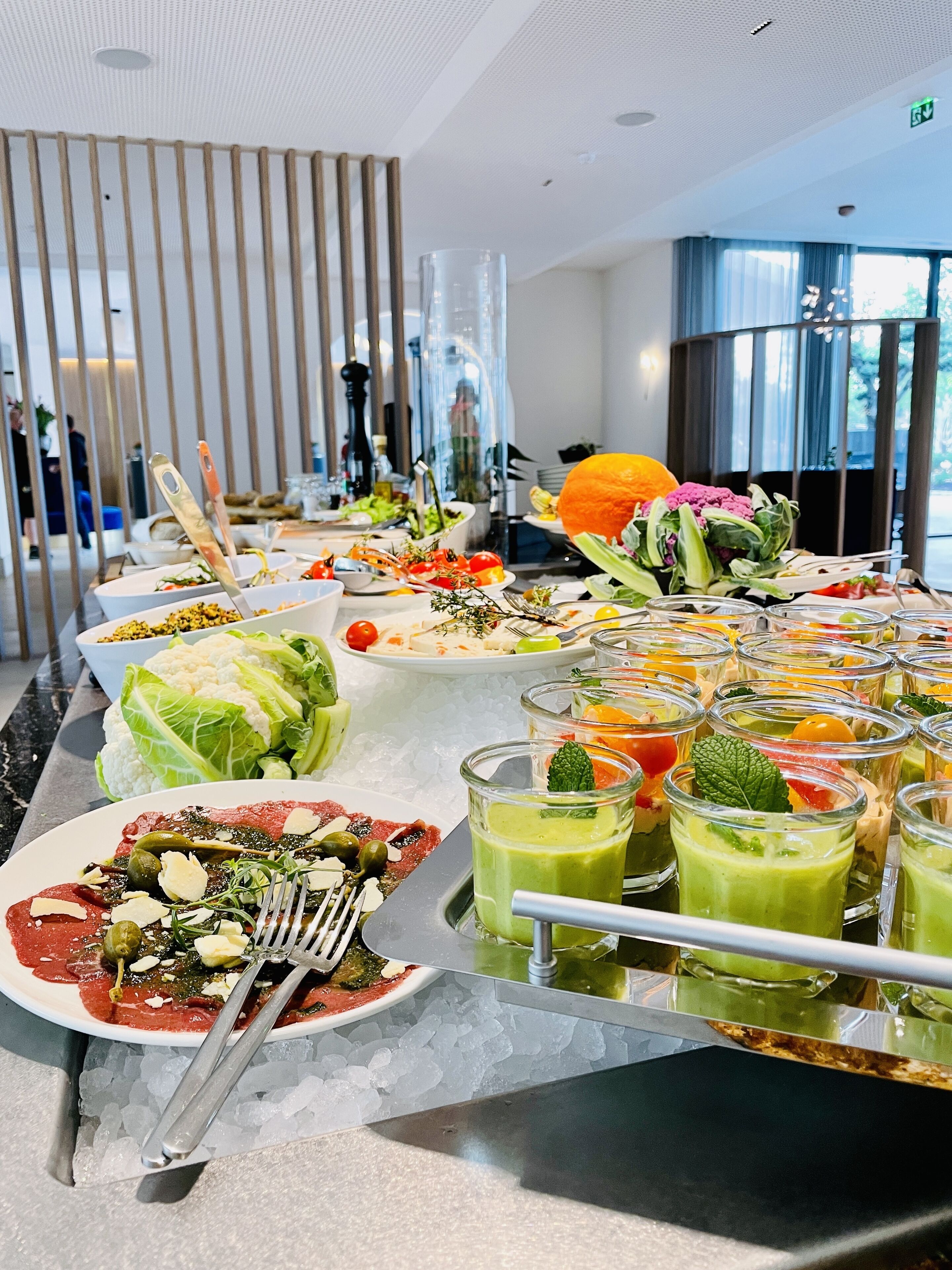 Un bufé con diversos platos y bebidas, entre ellos ensaladas, verduras y un batido verde.