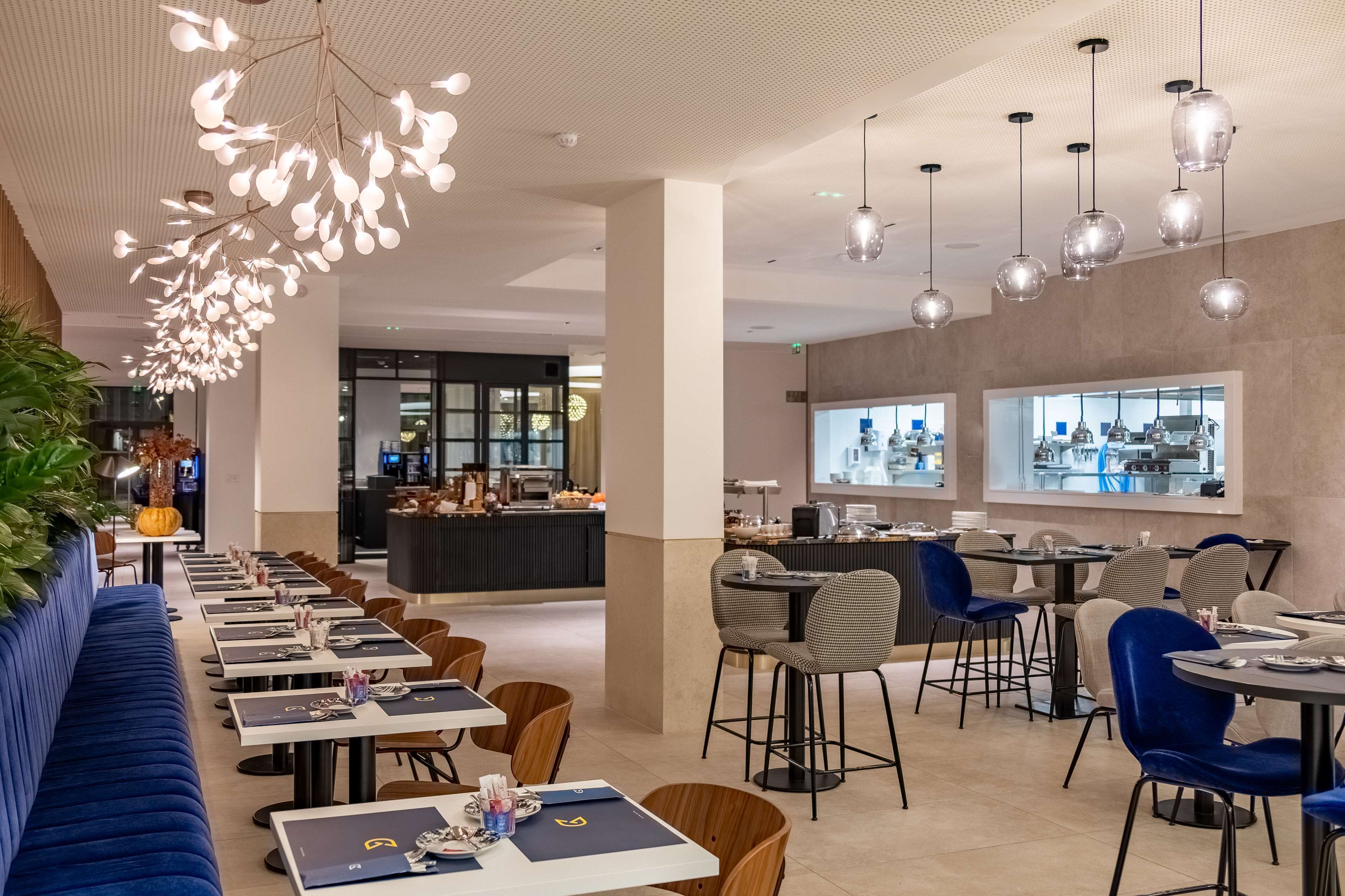 Un restaurant modern amb una barra llarga, seients blaus i llums penjants.