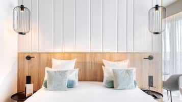 A modern hotel room with a large bed, two bedside tables, a wooden headboard, and two pendant lights.