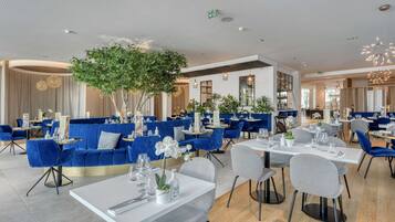 Un restaurante moderno con asientos azules, mesas blancas y un árbol central.