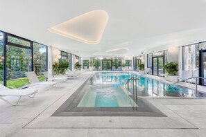 An indoor swimming pool with clear blue water, surrounded by white lounge chairs and potted plants. - Golden Tulip Lyon Ouest Techlid - Hotel and Spa (Limonest)
