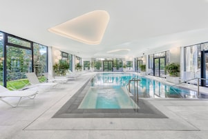 Una piscina interior con agua cristalina azul, rodeada de sillones blancos y plantas en macetas.