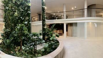 Een ruime atrium met een centrale tuin, gebogen witte muren en een glazen balustrade met uitzicht op de verdieping beneden.