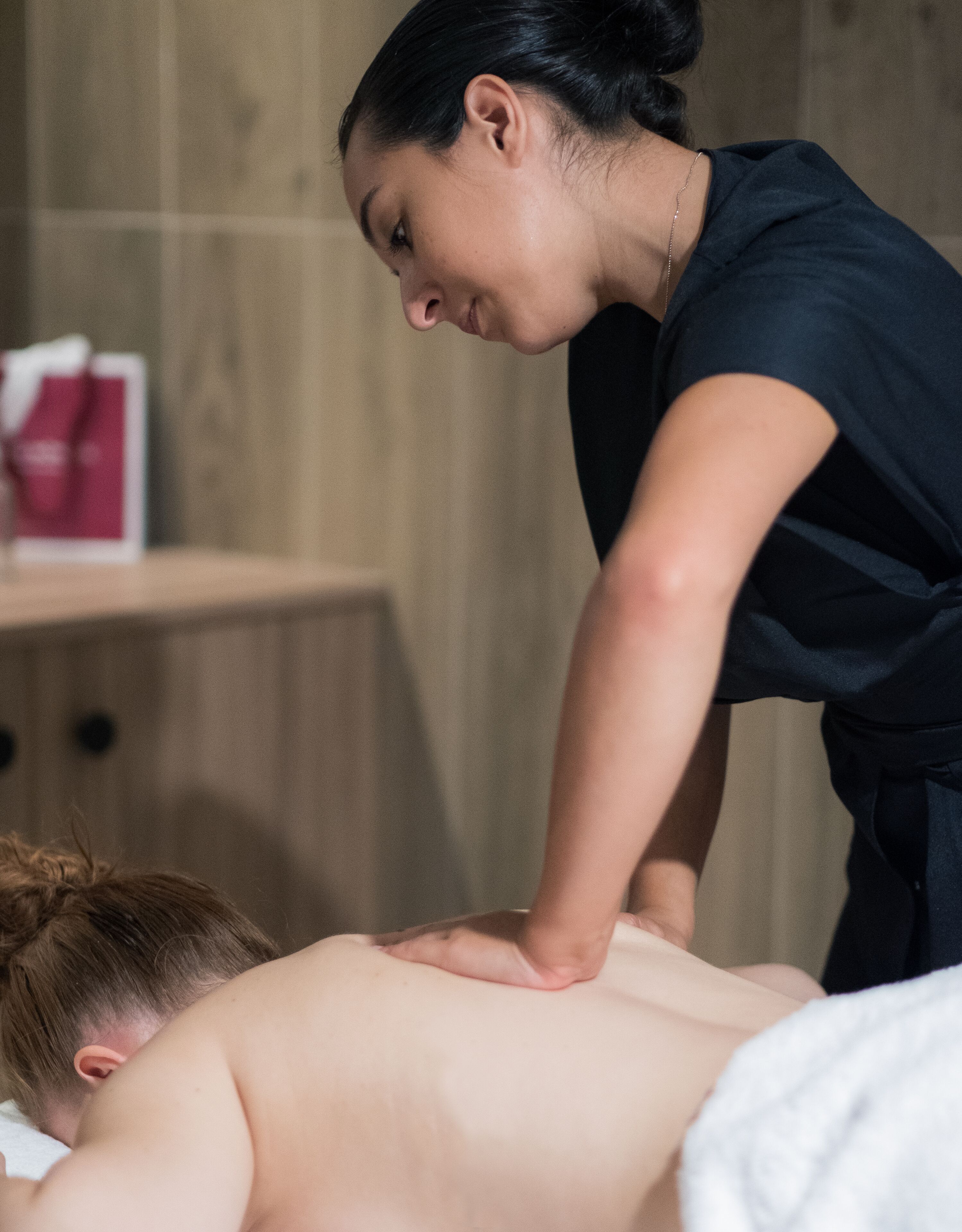 A person receiving a back massage in a room with wooden walls and a small table with a red object on it.