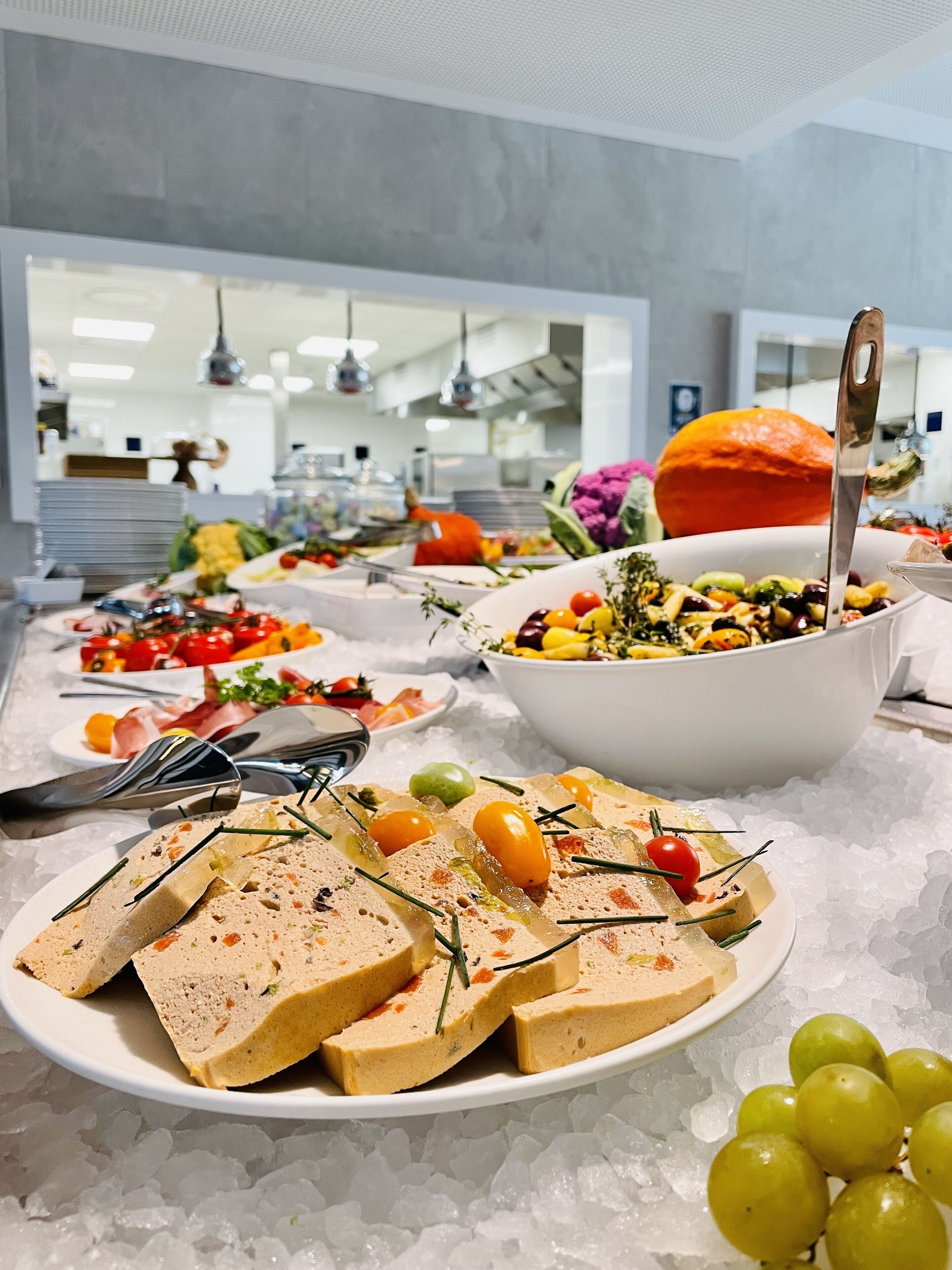 A buffet with various dishes, including a large bowl of salad, a plate of sliced meat, and a plate of cheese.