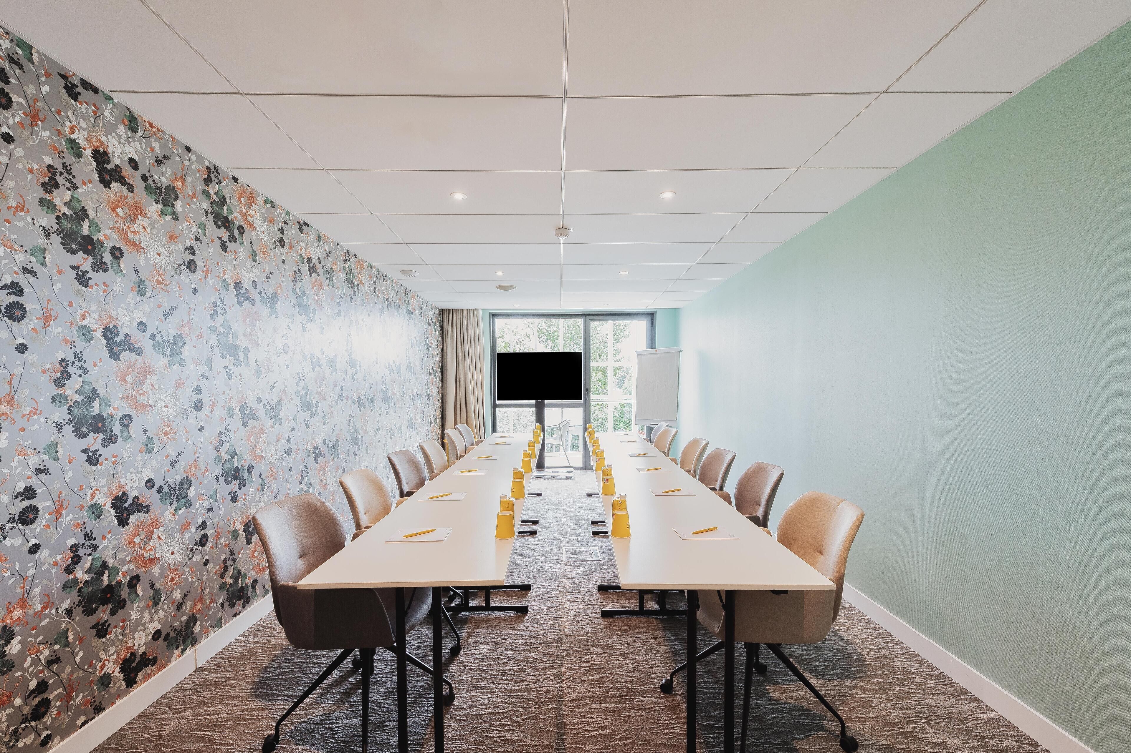 A conference room with a long table, chairs, and a floral-patterned wall.