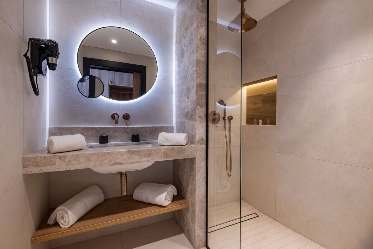 A modern bathroom with a marble sink, a hairdryer mounted on the wall, a mirror, and a glass-enclosed shower area.