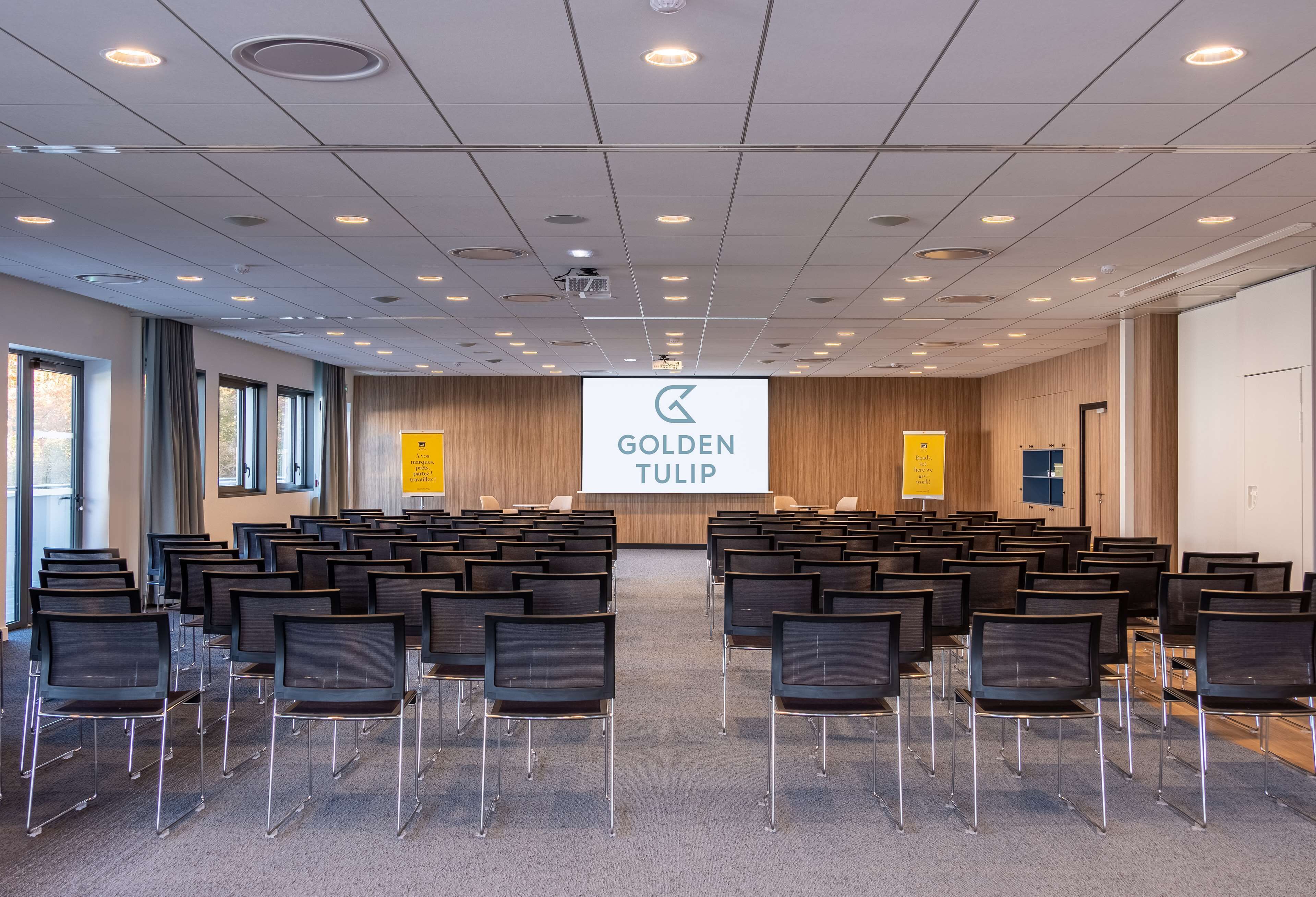 Un salón de conferencias con filas de sillas orientadas hacia una pantalla que muestra 