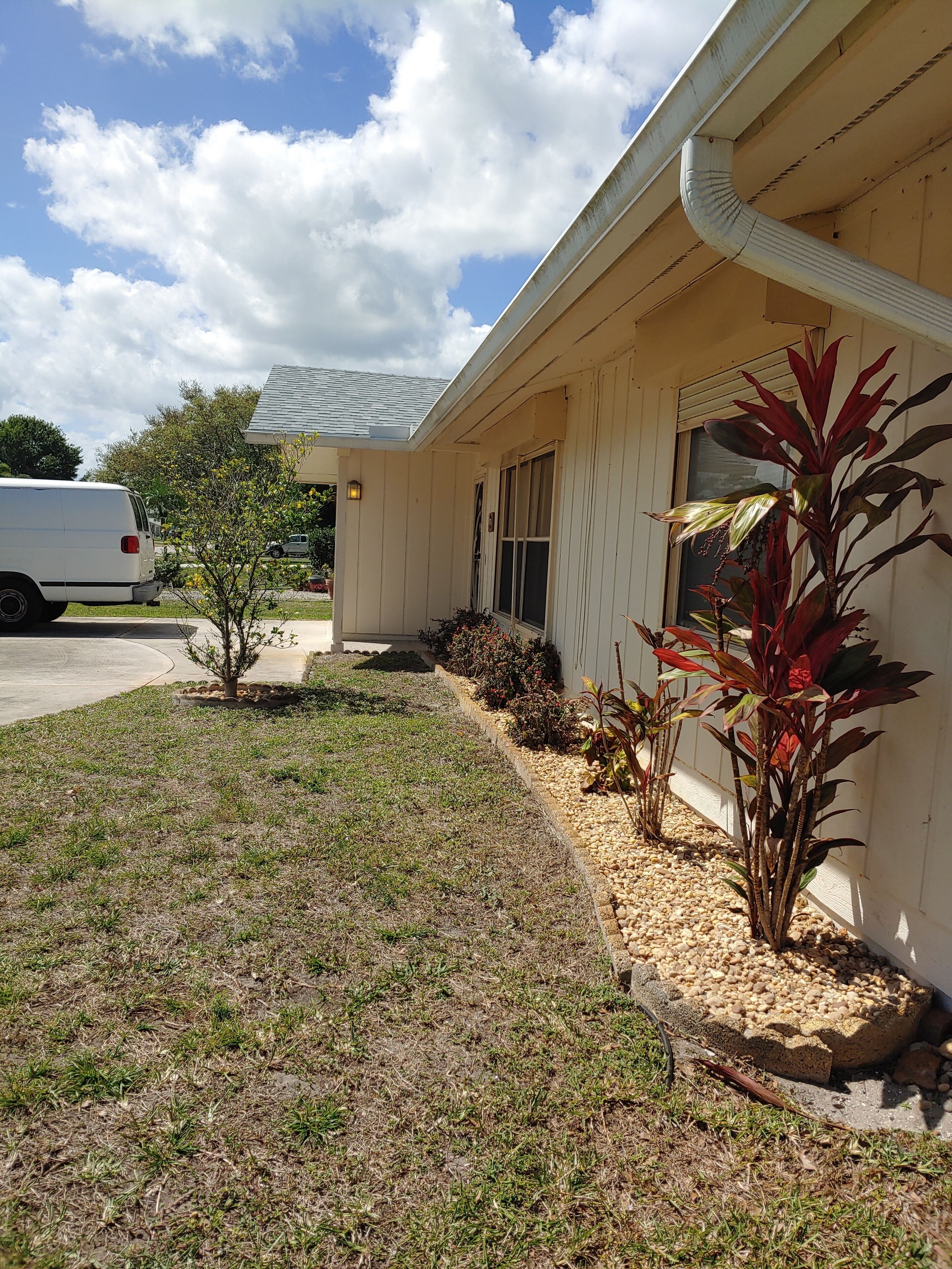 A single-story house with a front porch, a driveway, and a small garden with various plants.
