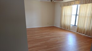 A room with wooden flooring, a ceiling fan, and a large window with curtains. - Split 2 bdrm/2 full bath floorplan, All new appliances, yearly rental (Stuart)