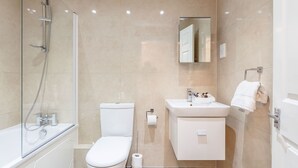 A modern bathroom with a glass-enclosed shower, a toilet, a sink, and a mirror. - Roomspace Apartments - Regents Court (Kingston Upon Thames)