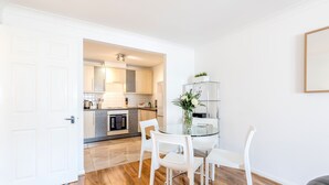 A modern kitchen with white cabinets, a glass dining table, and chairs. - Roomspace Apartments - Regents Court (Kingston Upon Thames)
