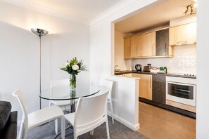 A modern kitchen with wooden cabinets, a stove, and a countertop with a kettle and toaster. - Roomspace Apartments - Regents Court (Kingston Upon Thames)