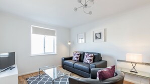 A modern living room with a leather sofa, a glass coffee table, and a flat-screen TV. - Roomspace Apartments - Regents Court (Kingston Upon Thames)