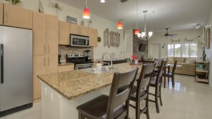A modern kitchen with granite countertops, stainless steel appliances, and wooden cabinets. There is a dining area with bar stools and a large island. The room has pendant lighting and a ceiling fan. - Perfect South Padre Island Getaway (South Padre Island)
