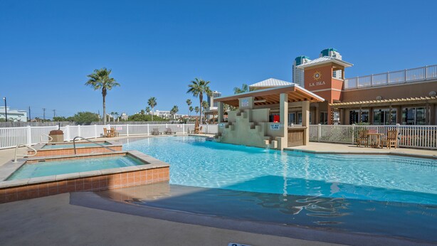 A swimming pool area with a lifeguard tower, palm trees, and a covered seating area. - Perfect South Padre Island Getaway (South Padre Island)