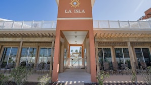 The entrance to La Isla with a sun logo, a covered walkway, and outdoor seating. - Perfect South Padre Island Getaway (South Padre Island)