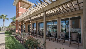 An outdoor patio with wooden chairs and tables, a pergola, and a poolside area with a view of the pool. - Perfect South Padre Island Getaway (South Padre Island)