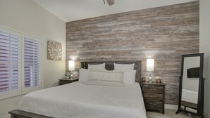 A bedroom with a wooden headboard, a large bed with white bedding, two bedside tables with lamps, a mirror, and a window with blinds. - Perfect South Padre Island Getaway (South Padre Island)