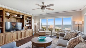 A spacious living room with a large television, wooden cabinets, a ceiling fan, and a view of the beach. - 5508 Hampton Place - UPDATED Villa with Fantastic Oceanfront Views! (Hilton Head Island)