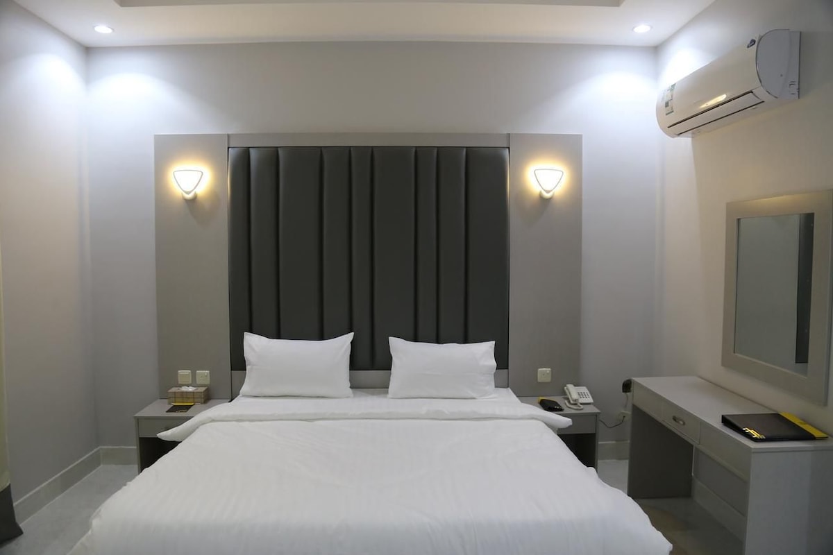 A modern hotel room with a large bed, two bedside tables, a desk, and a mirror.