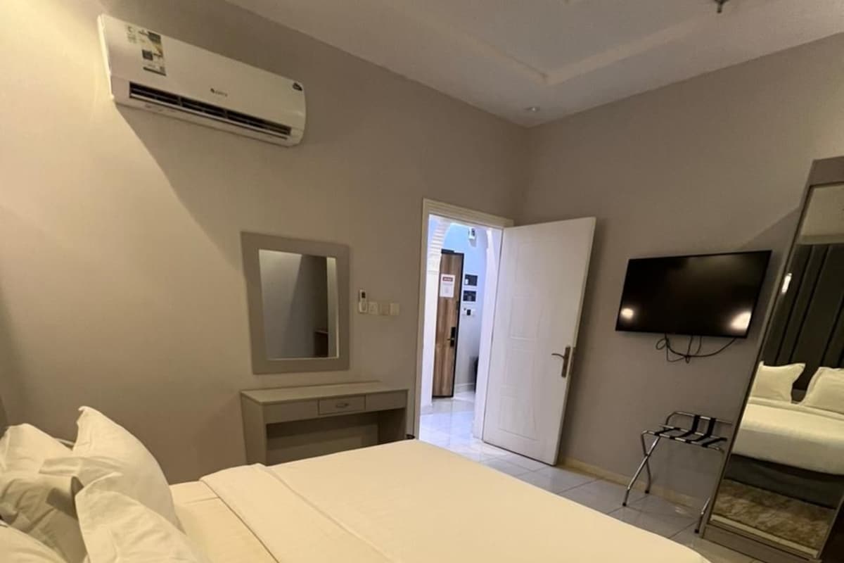 A hotel room with a bed, a TV, an air conditioning unit, a wardrobe, and a mirror.