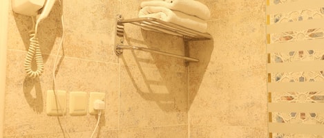 A bathroom with a hairdryer mounted on the wall, a towel rack with folded towels, and a patterned tile backsplash.