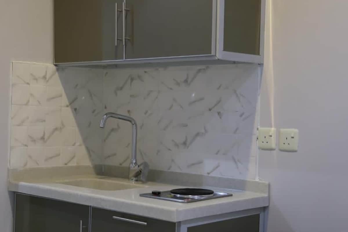 A compact kitchen with a sink, cabinets, and a trash bin.