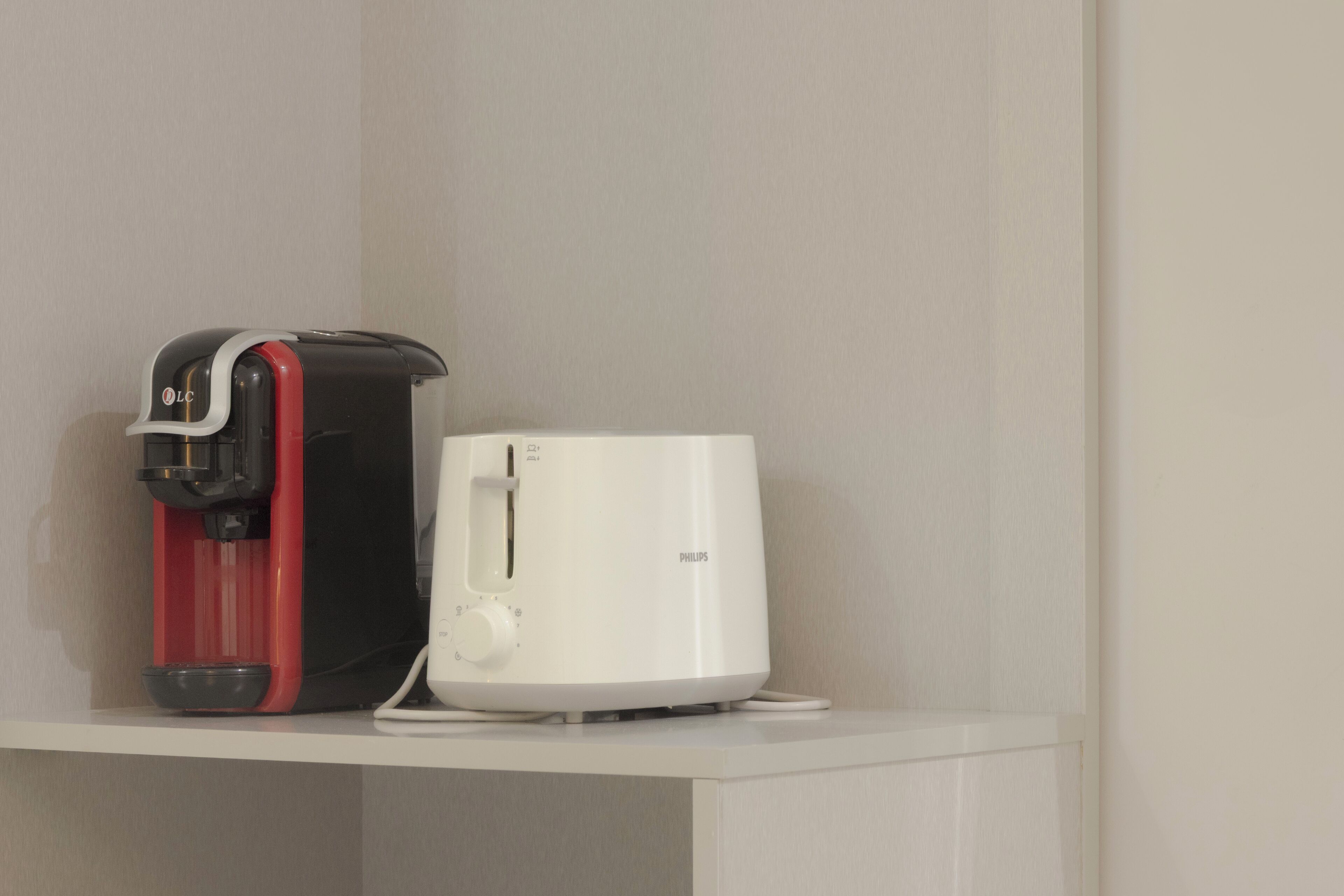 A coffee maker and a white appliance on a white shelf.