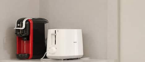 Una macchina da caffè e un elettrodomestico bianco su uno scaffale bianco, su uno sfondo neutro.