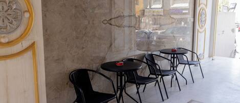 A cafe with marble walls, a 'Smoking Area' sign, and black metal chairs around small tables.