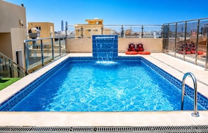 A rooftop swimming pool with a blue mosaic border, a water feature, and a view of the cityscape. -  Areen Alnaeem Hotel (Jeddah)