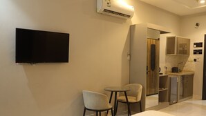 A hotel room with a flat-screen TV mounted on the wall, a small round table with two chairs, a minibar, and a bathroom visible through an open door. -  Areen Alnaeem Hotel (Jeddah)