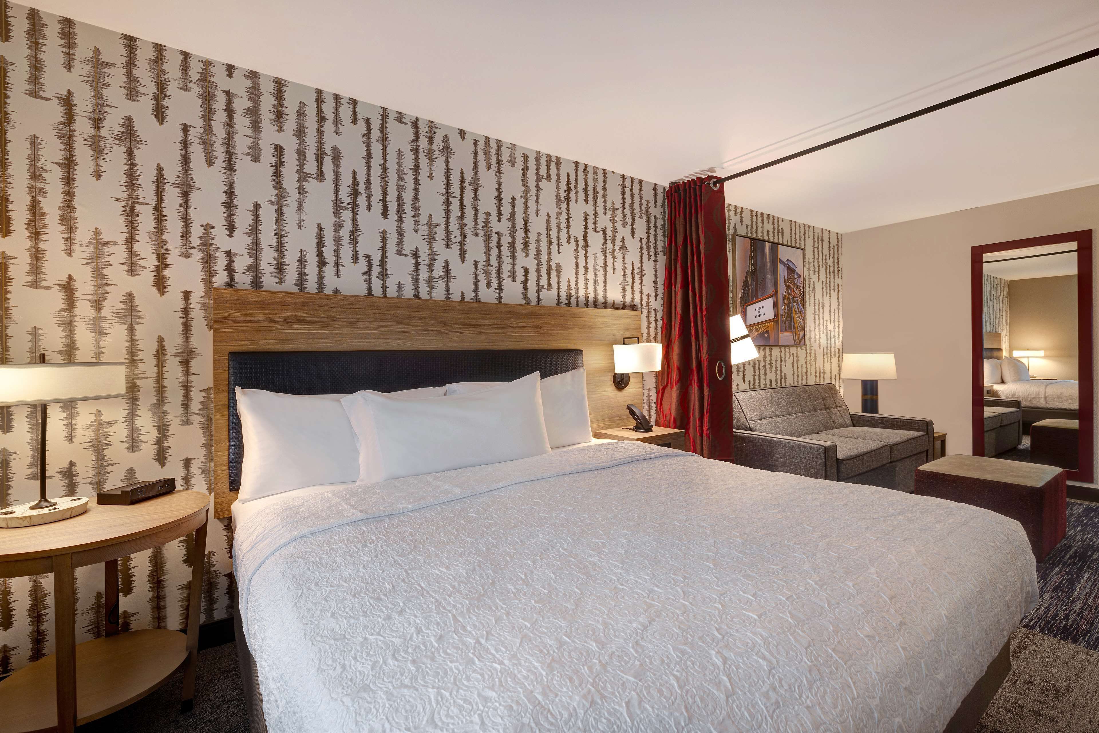 A hotel room with a large bed, two bedside tables with lamps, a chair, and a mirror.