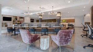 A modern hotel lobby with a central seating area, a bar, and a television screen. - Home2 Suites by Hilton Anderson Downtown (Anderson)