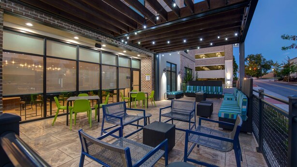 An outdoor patio area with seating arrangements, including chairs and tables, and a covered section with a view of the street. - Home2 Suites by Hilton Anderson Downtown (Anderson)