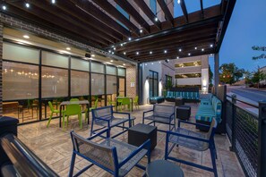 An outdoor patio area with seating arrangements, including chairs and tables, and a covered section with a view of the street.