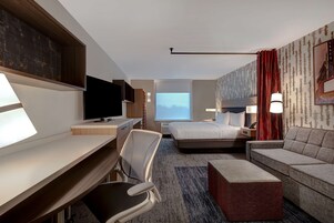 Una habitación de hotel con escritorio, silla, cama, sofá y televisor.